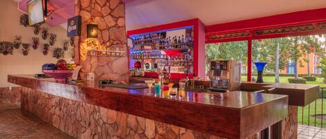 Una zona de bar con mostrador de piedra, estanterías llenas de botellas de licor y un televisor en la pared.