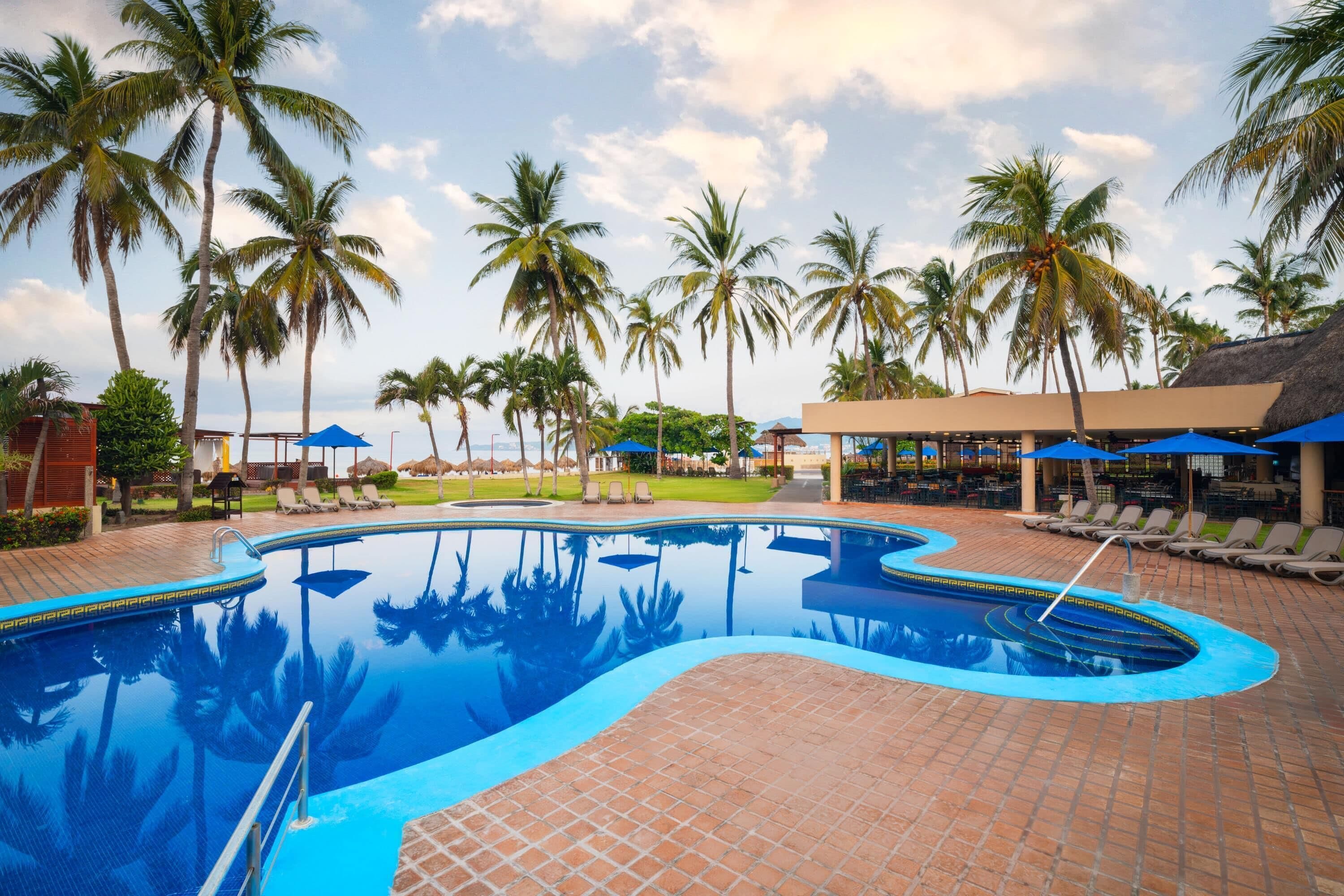 Une piscine dotée d’une terrasse carrelée, entourée de palmiers et de chaises longues.