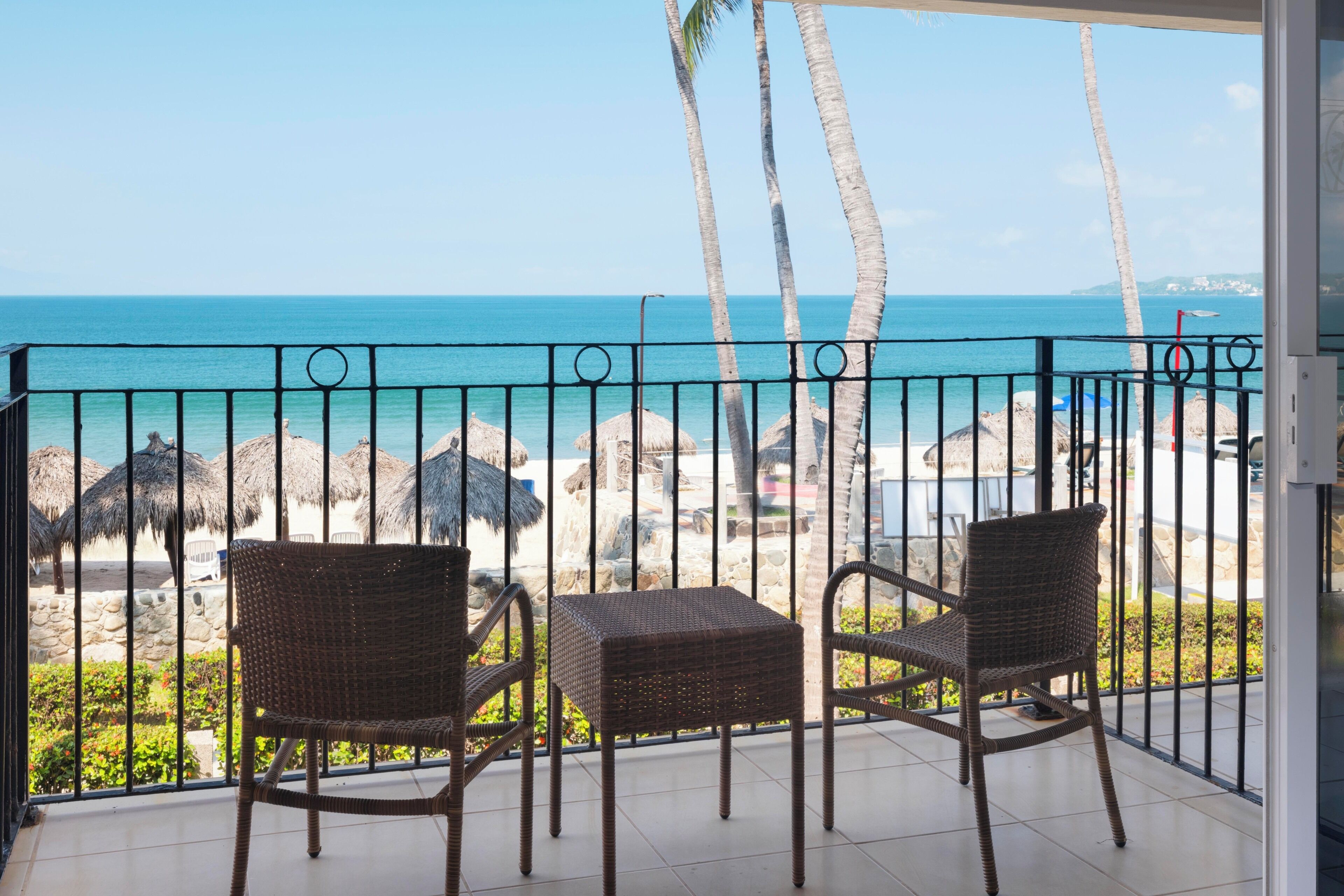 Un balcon avec des fauteuils en osier et une vue sur la plage et l’océan.