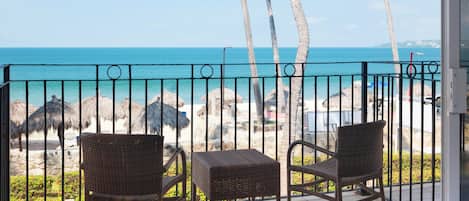 A balcony with wicker chairs and a view of the beach and ocean.