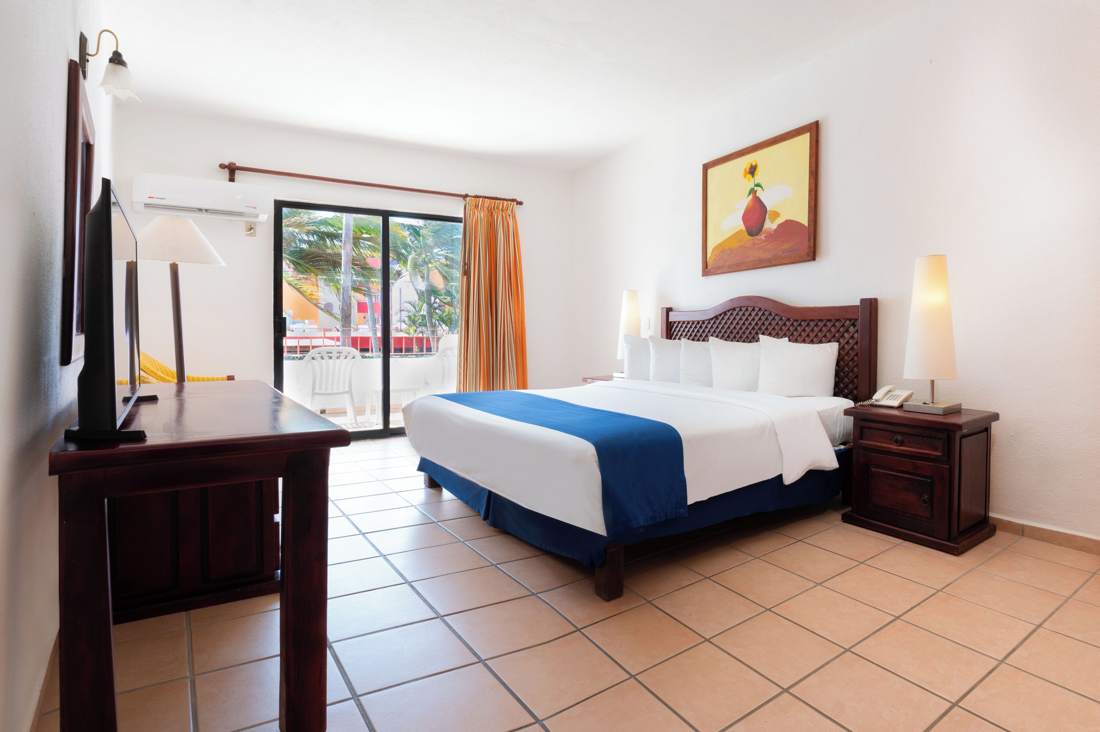 A hotel room with a bed, bedside table, lamp, air conditioning unit, and a view of the outside.