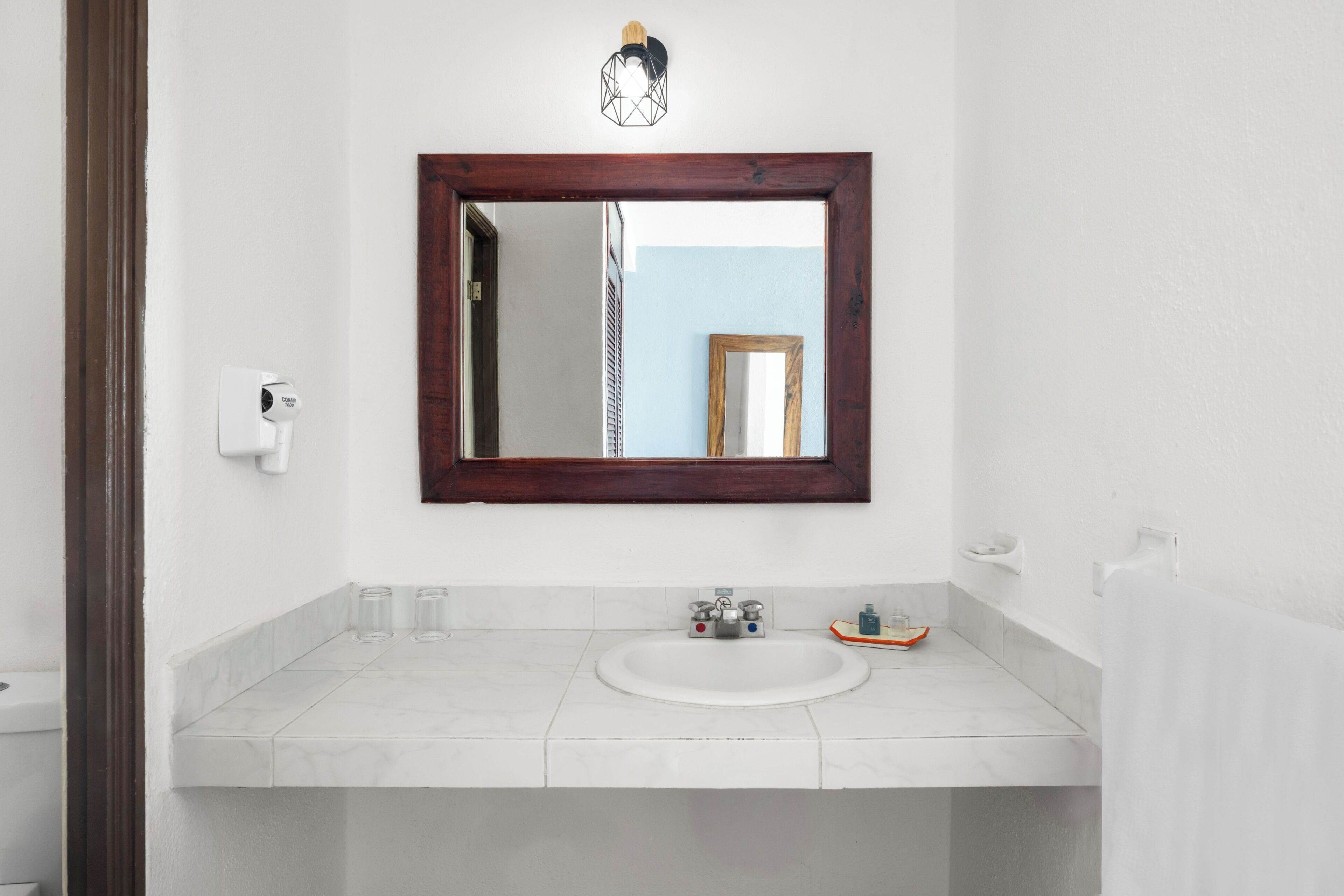 Ein Badezimmer mit einem weißen Waschbecken, einem spiegel mit Holzrahmen und einem Handtuchhalter.