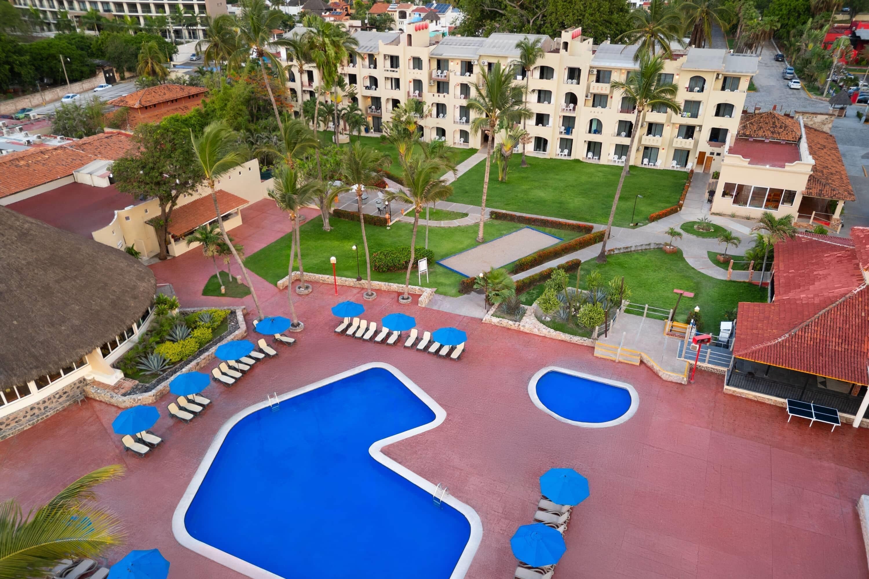 Un resort con varias piscinas, palmeras y un edificio grande con balcones.