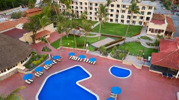 Un resort con varias piscinas, palmeras y un edificio grande con balcones.