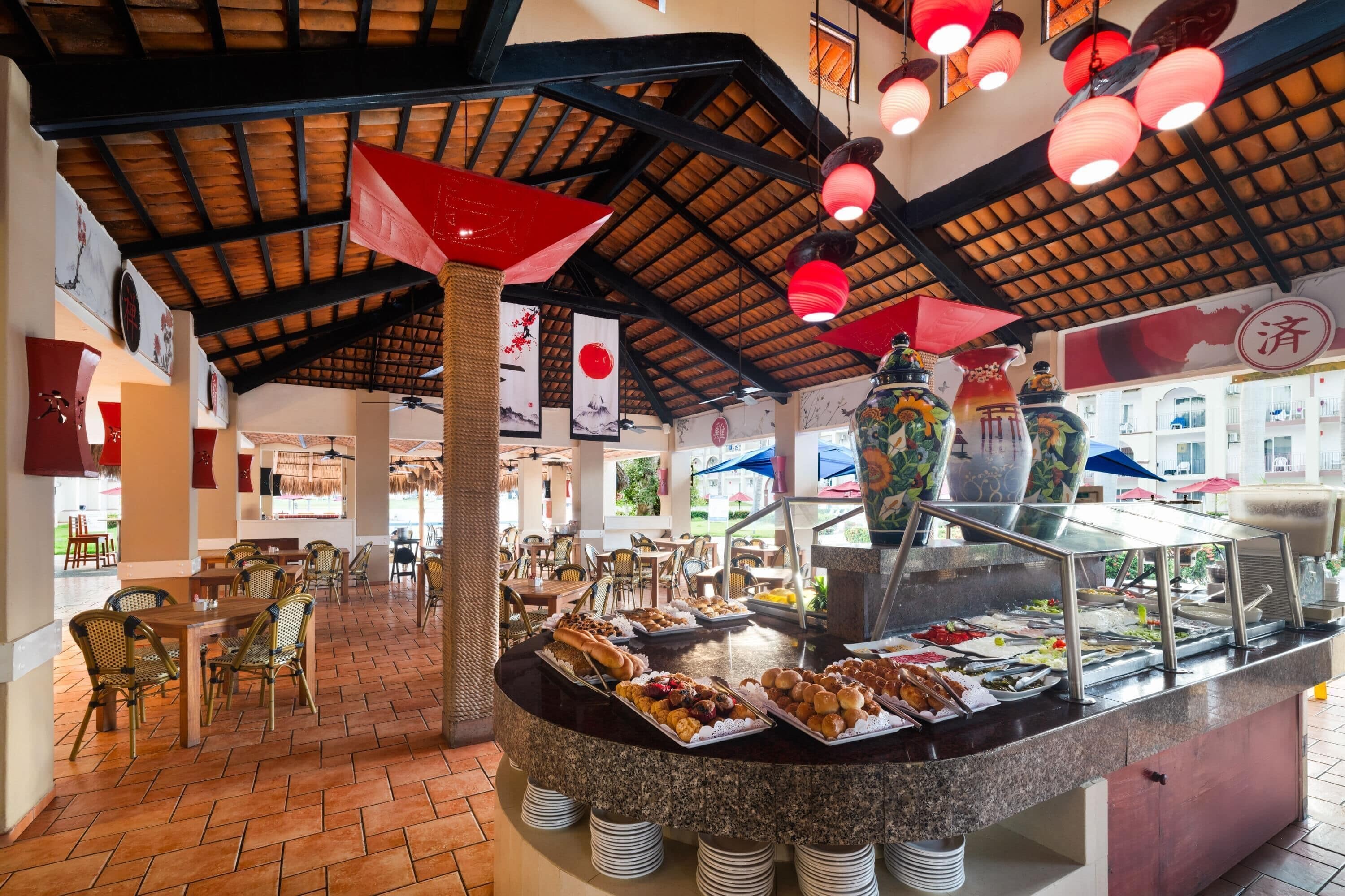 Zona de buffet amb diverses opcions gastronòmiques, un disseny de sostre tradicional i una zona de seients amb cadires i taules.