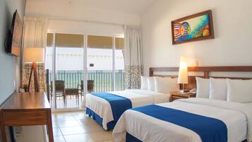 Habitación de hotel con dos camas, un escritorio, una silla, un balcón con vistas y un cuadro en la pared.