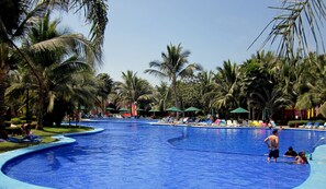 A large outdoor swimming pool surrounded by palm trees and lounge chairs.