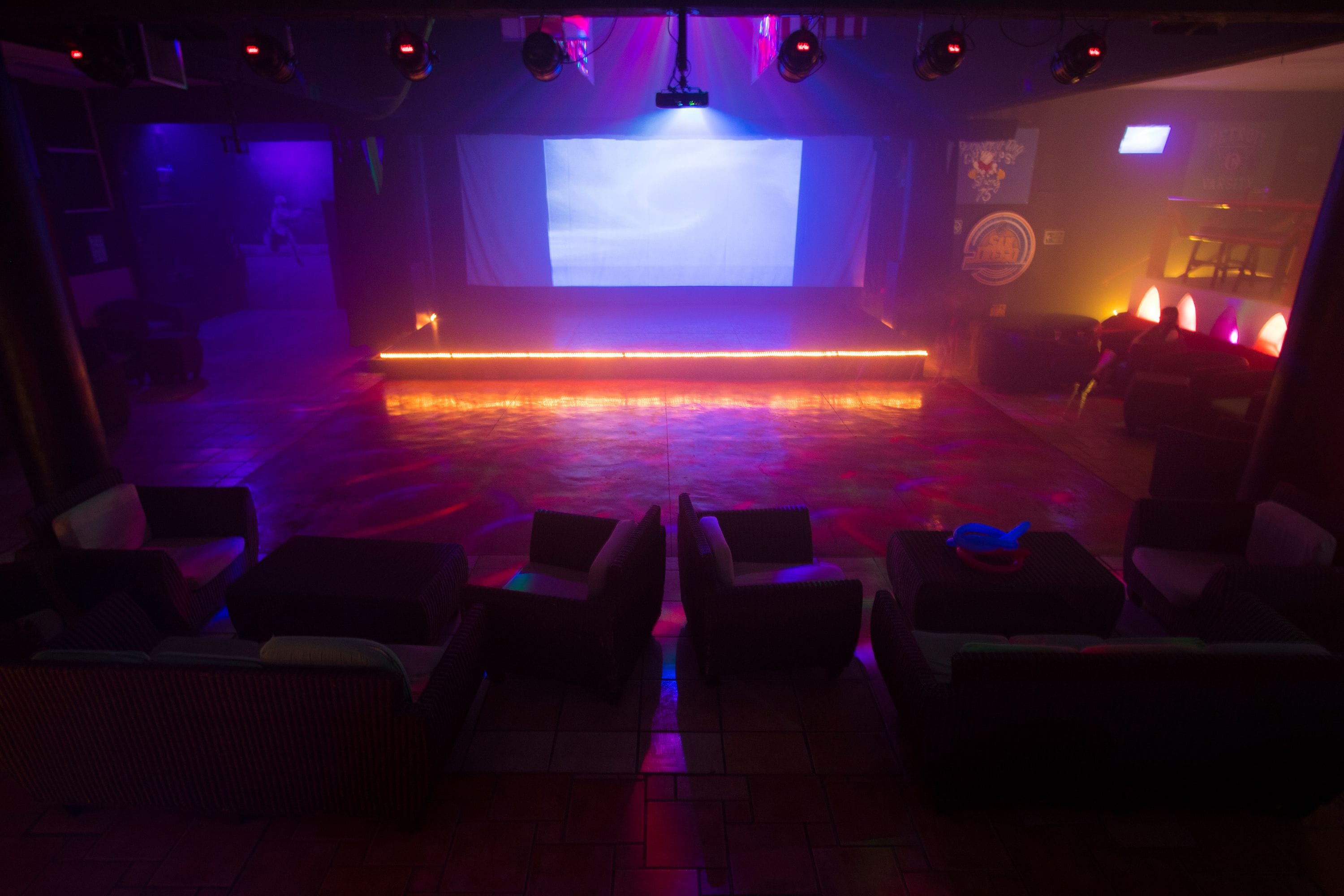 Una sala tenuemente iluminada con un escenario, zona de asientos y una pantalla grande.