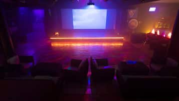 Una sala tenuemente iluminada con un escenario, zona de asientos y una pantalla grande.