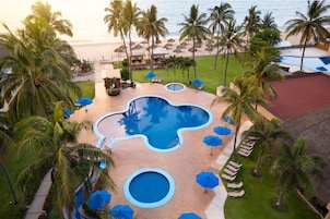 Zona de piscina en un resort, con varias piscinas, palmeras y sombrillas de playa.