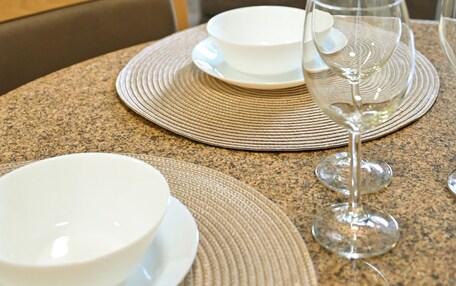 A hotel room with a dining table set with plates and wine glasses, a bed, a lamp, and curtains.