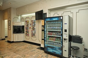 A hotel lobby with a vending machine, a television mounted on the wall, and a seating area with a small table and chair.