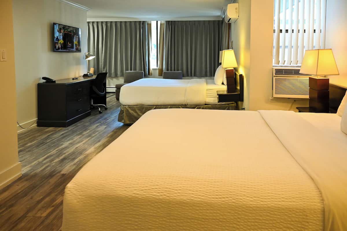 A hotel room with a large bed, a desk with a chair, a TV, and a window with curtains.