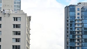 Un edificio alto con muchas ventanas, vista a una masa de agua y un horizonte urbano lejano.