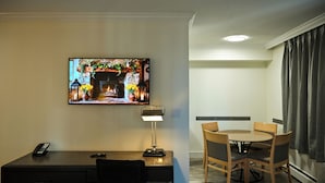 Habitación de hotel con escritorio, silla, mesa de comedor y sillas. Un televisor montado en la pared muestra una escena de chimenea.