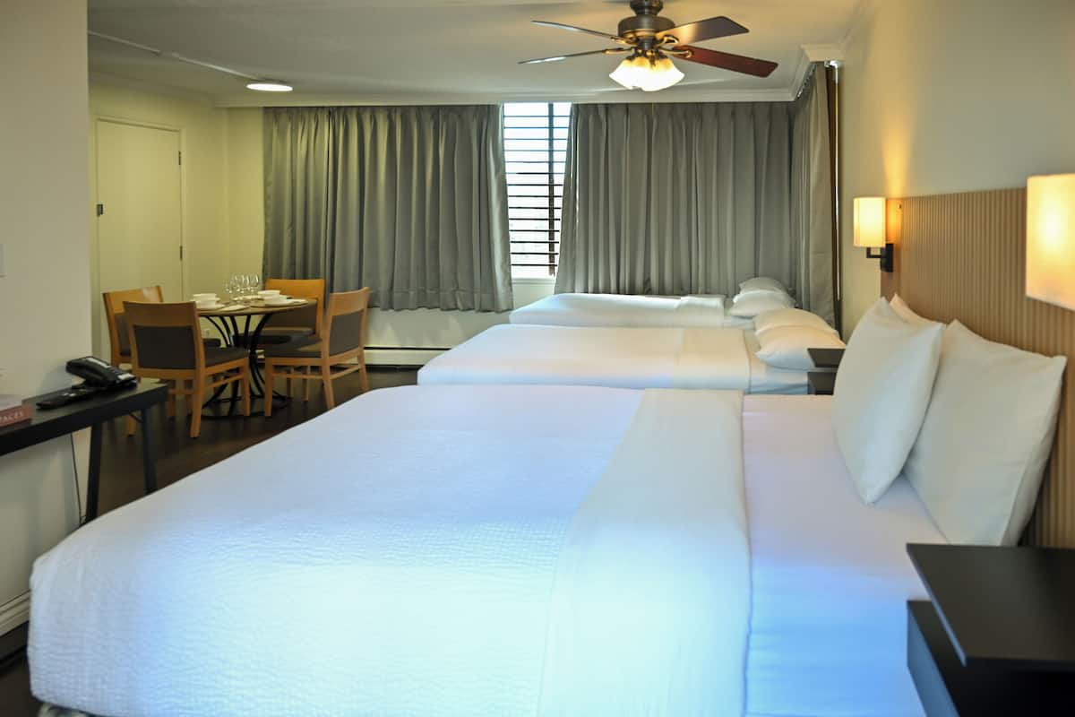 A hotel room with two beds, a desk with a chair, a ceiling fan, and a window with curtains.