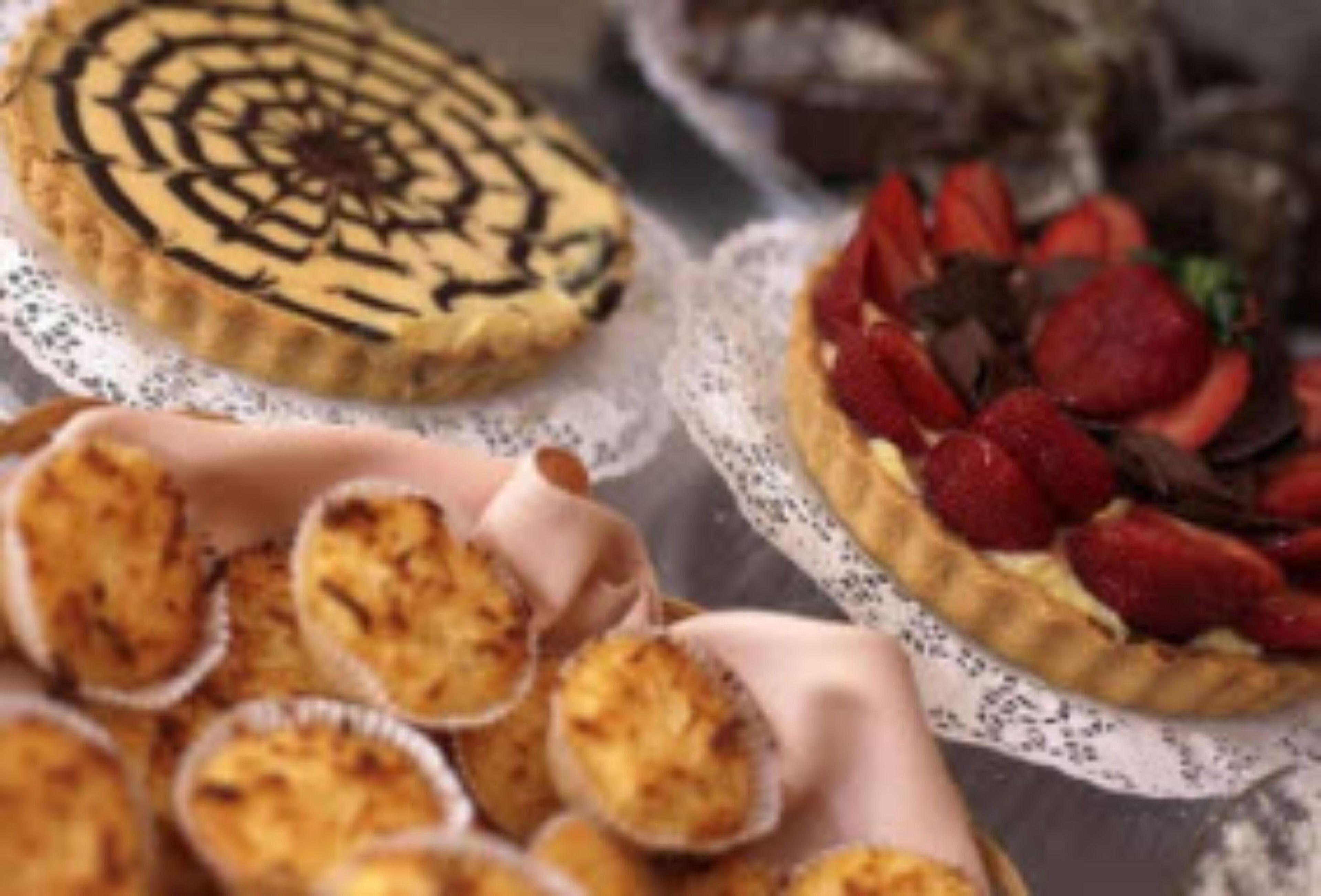 Diversos postres, incluyendo una tarta con diseño en espiral, una tarta con fresas y tartaletas mini.
