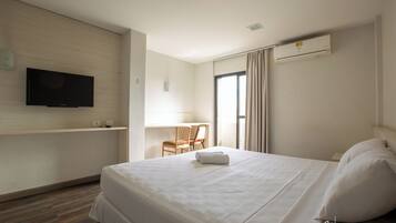 Quarto de hotel com uma cama, uma televisão fixada na parede, uma escrivaninha com cadeira e um ar condicionado.