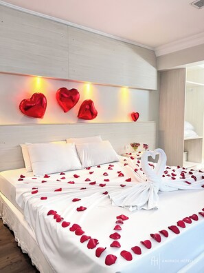 A hotel room with a neatly made bed, white linens, rose petals, and heart-shaped decorations on the wall. - Rede Andrade Vernon (Curitiba)