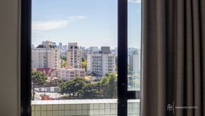 Vista desde una ventana con cortinas, que muestra un paisaje urbano con diversos edificios y un cielo despejado.