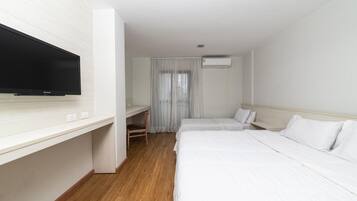 A hotel room with a flat-screen TV, a desk, two beds, a window with curtains, and an air conditioning unit.