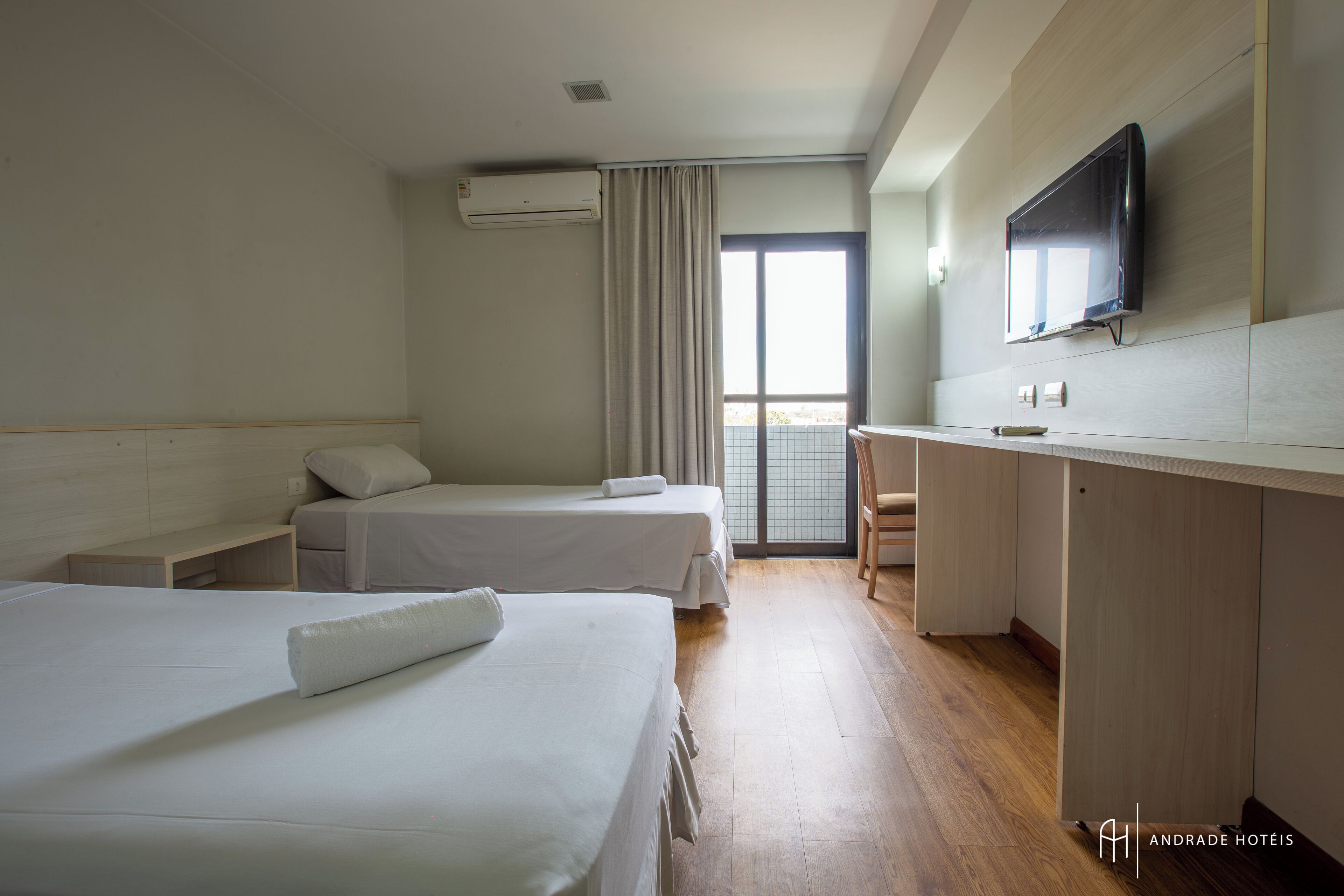 A hotel room with two beds, a desk, a TV, and a window with curtains.