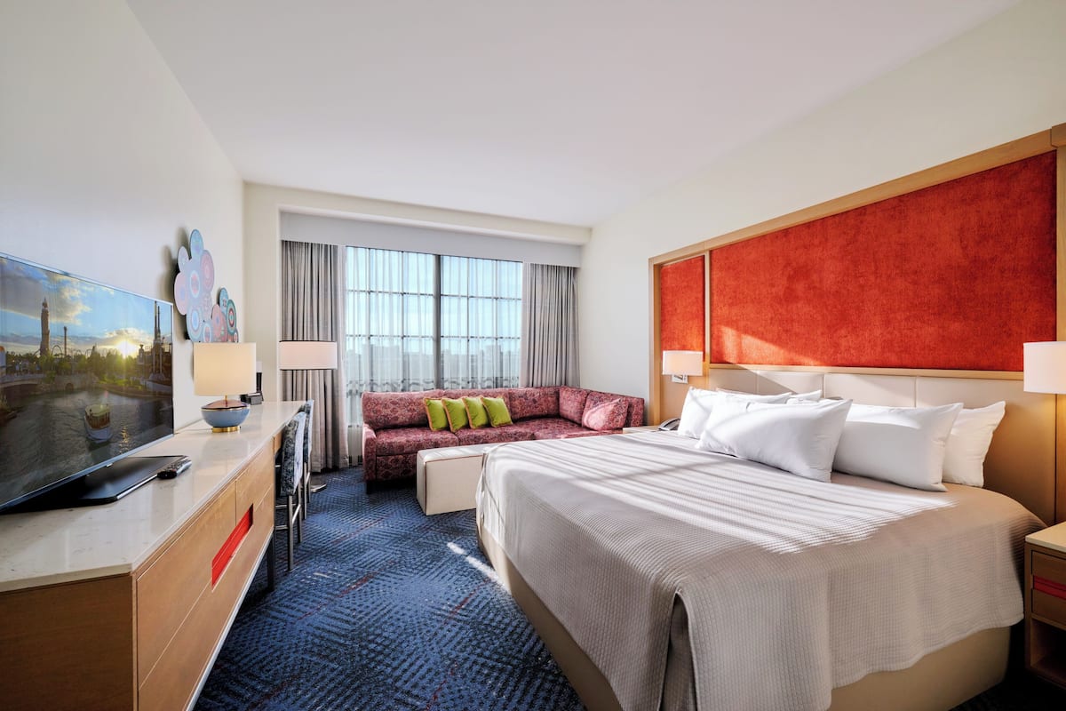 A hotel room with a large bed, a sofa, a TV, and a window with curtains.
