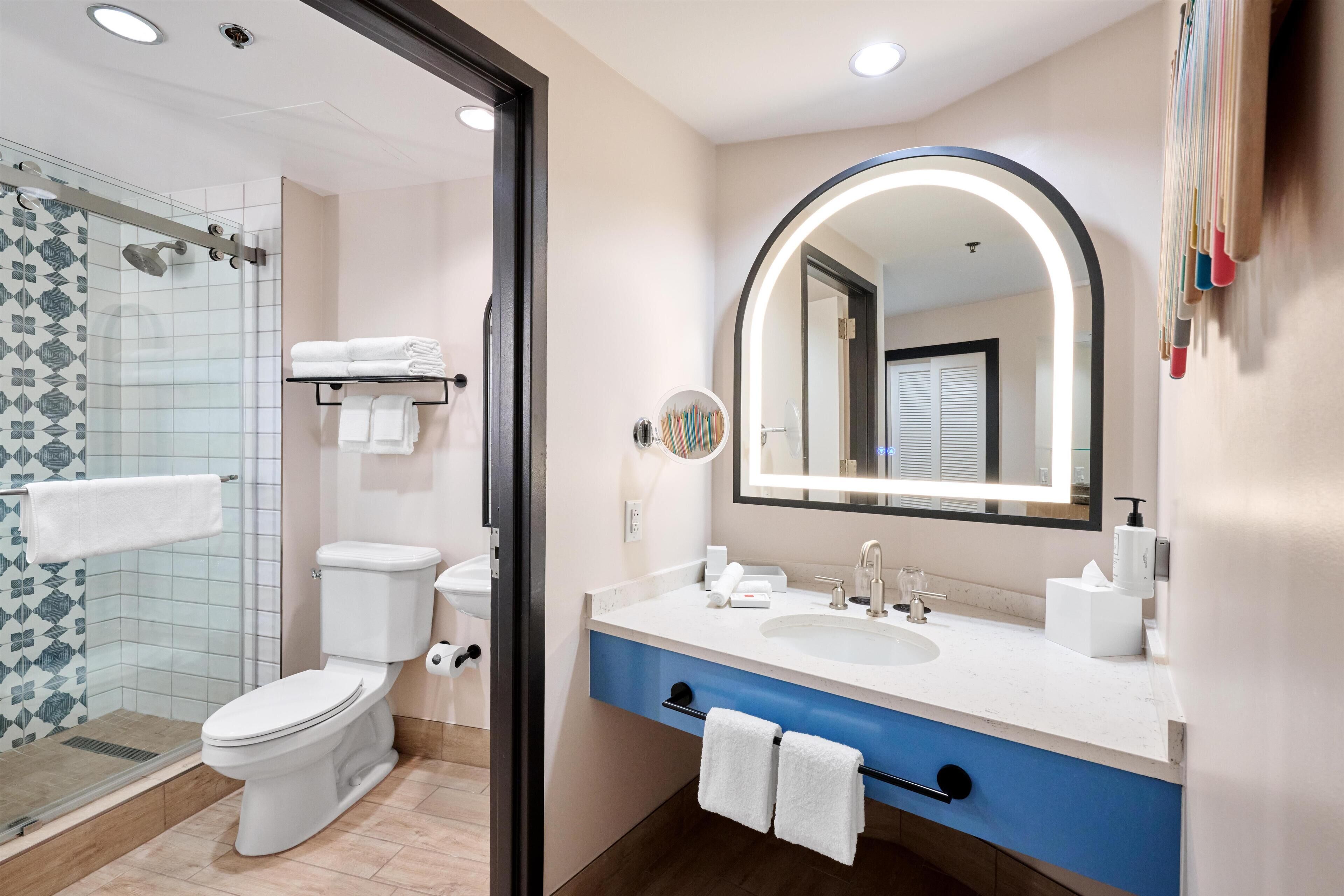 Un baño moderno con cabina de ducha de vidrio, inodoro, lavabo con espejo y toallero.