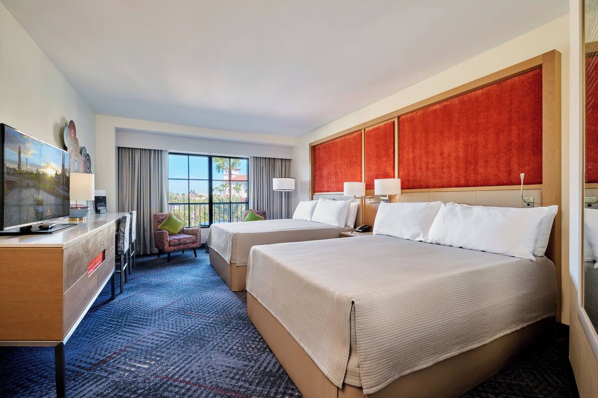 A hotel room with two beds, a desk, a chair, and a TV.