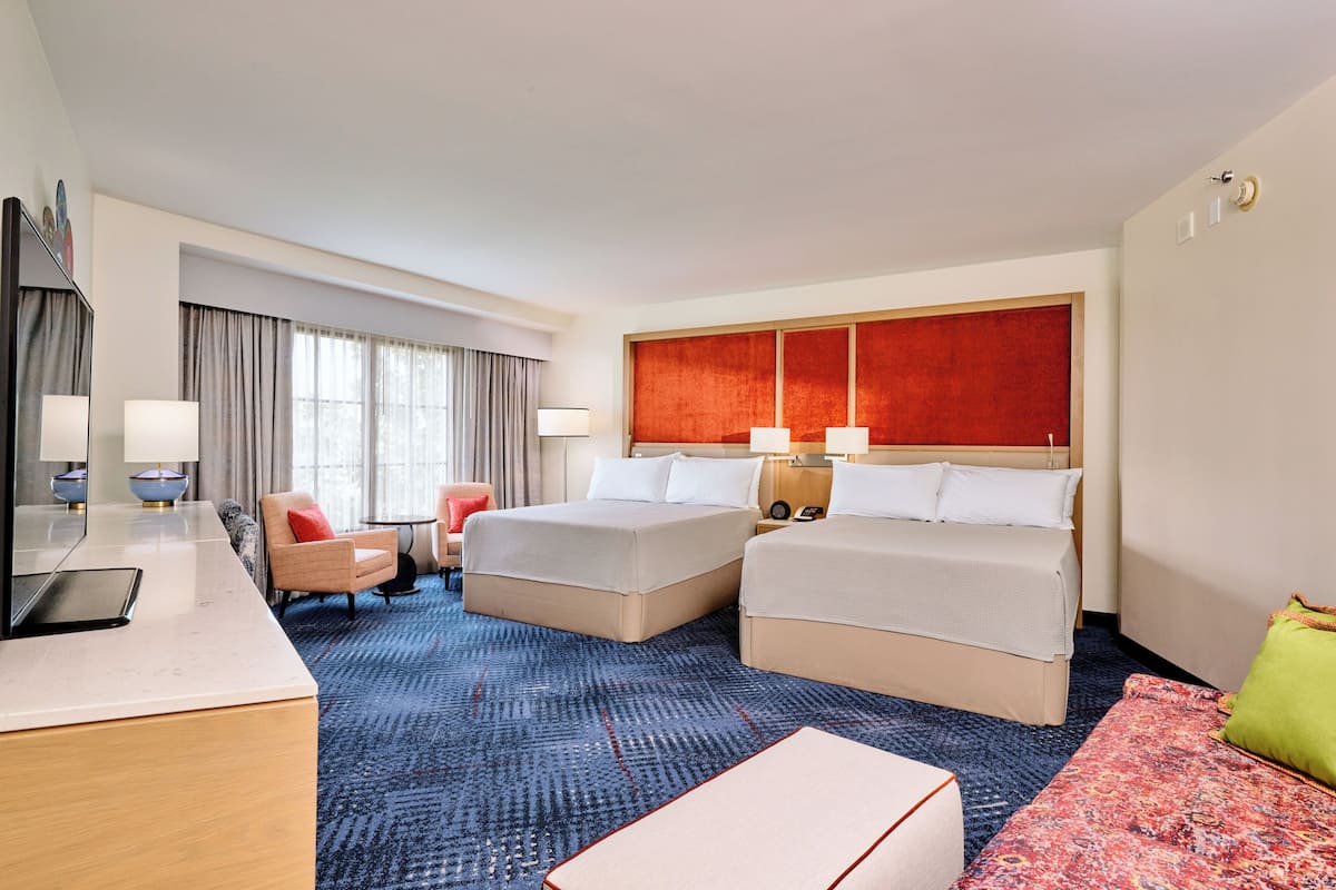 A hotel room with two beds, a desk, a chair, and a large window with curtains.