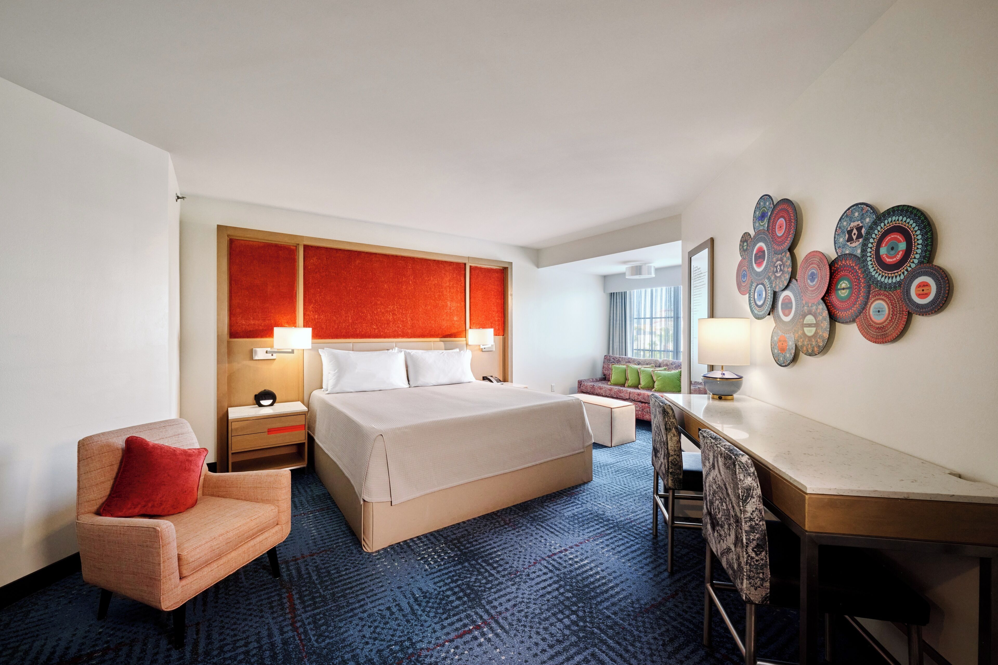 Une chambre d’hôtel avec un grand lit, un bureau, une chaise, une table de chevet et un mur décoré d’assiettes.