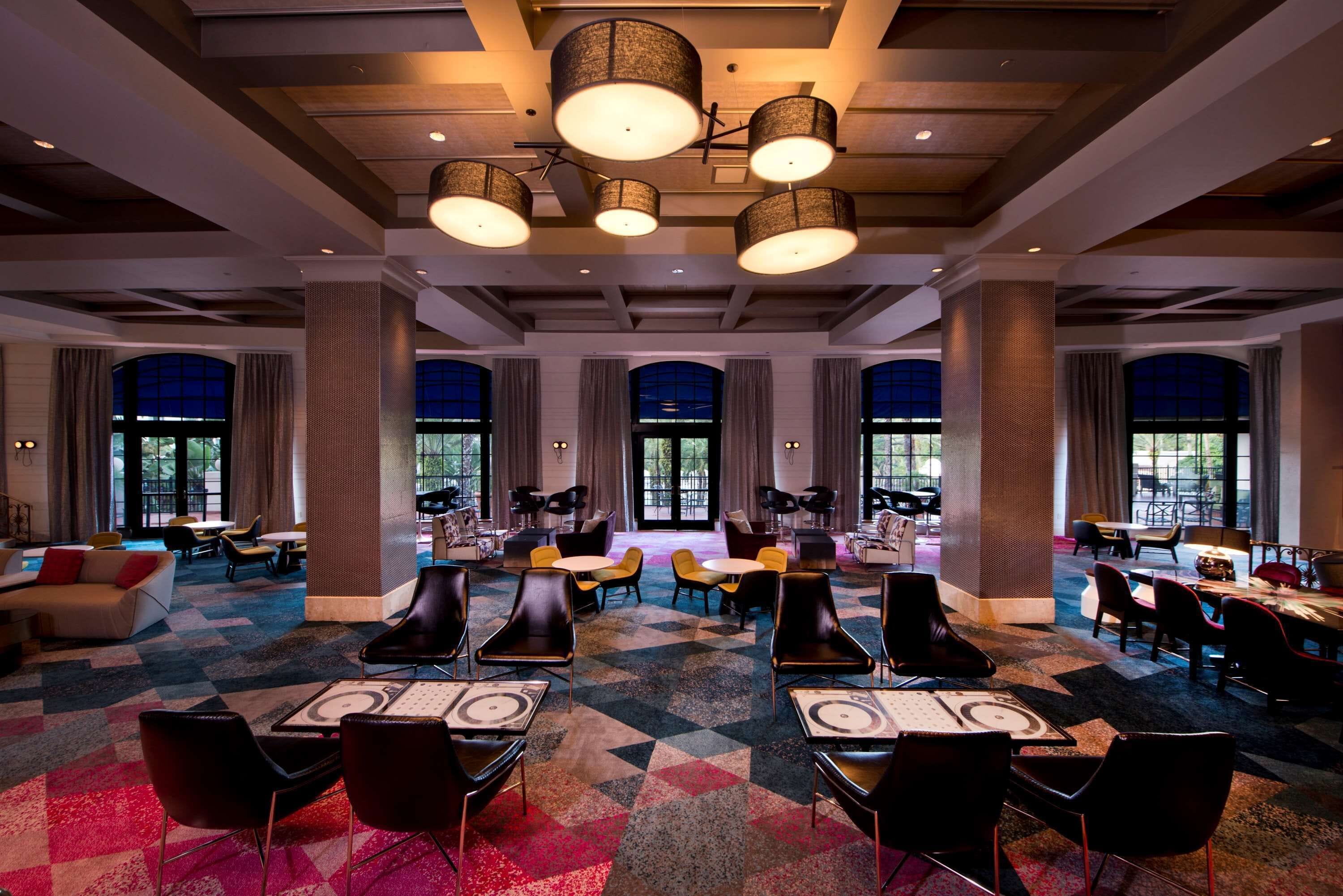 A spacious hotel lobby with multiple seating areas, large windows, and modern lighting fixtures.