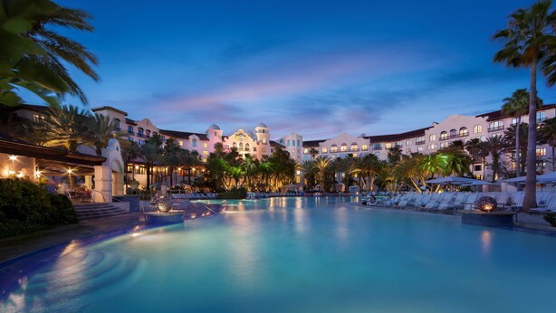 A large swimming pool with lounge chairs and palm trees, surrounded by hotel buildings with arched windows and a central dome structure. - Universal's Hard Rock Hotel (Orlando)