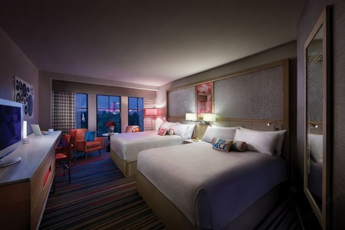 Habitación de hotel con dos camas, un escritorio, un televisor y vista a la ciudad.
