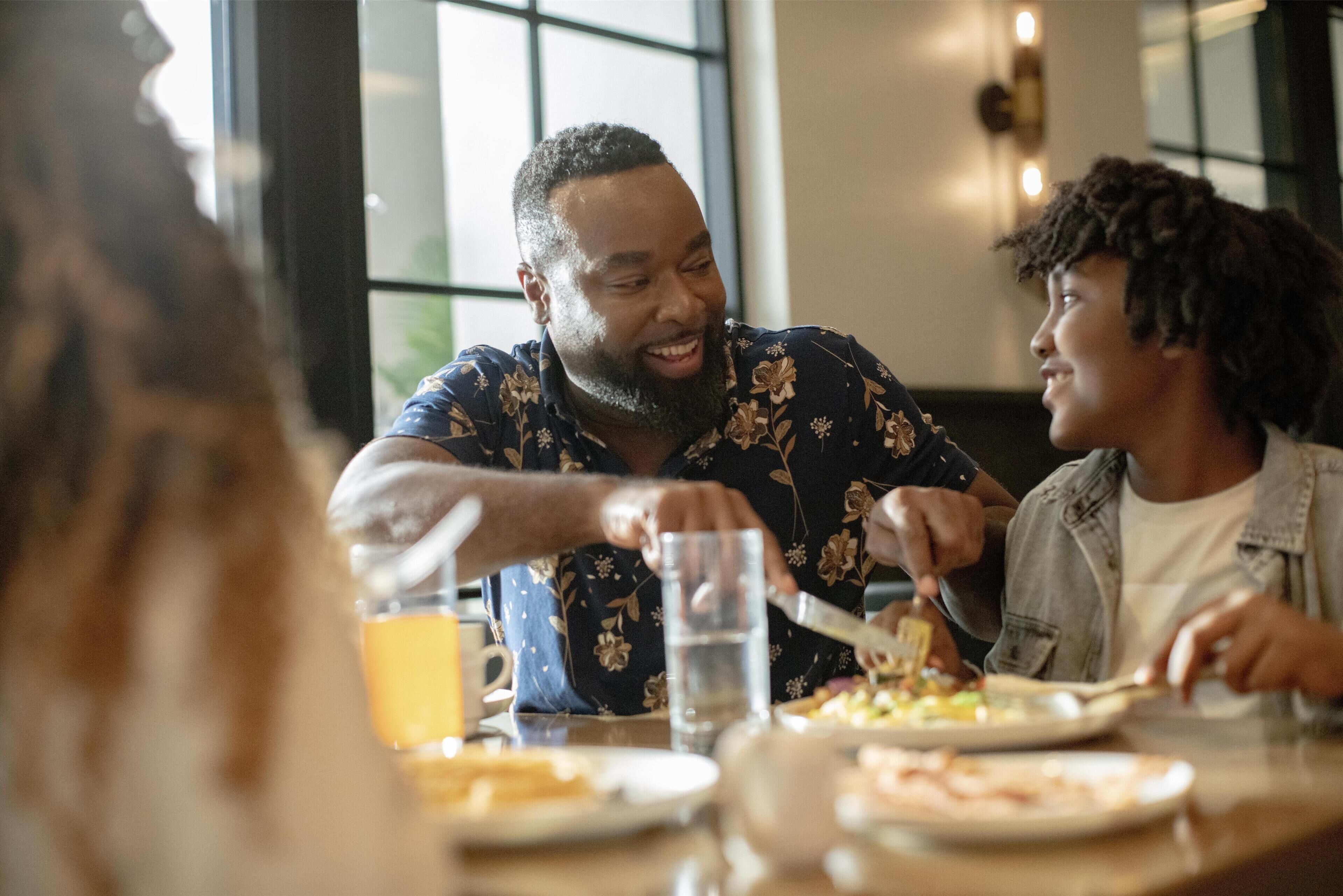 A dining table with plates of food, glasses, and a person serving food.