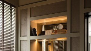 Una habitación con una mesa redonda, dos sillas estampadas, una lámpara y una ventana con persianas.