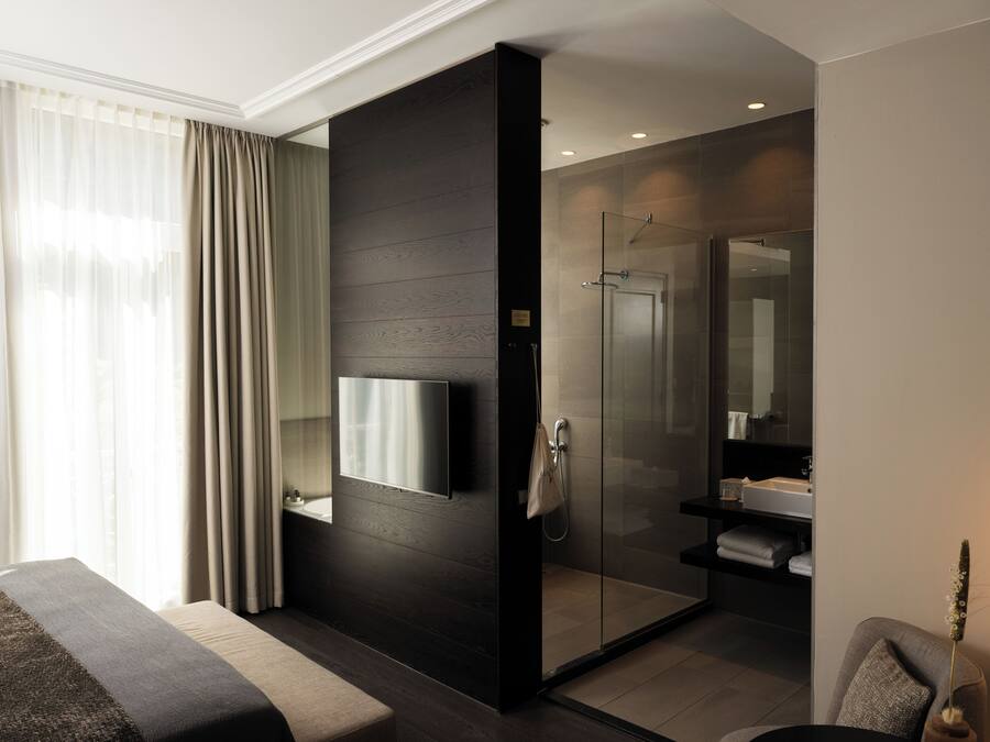 A modern hotel room with a large bed, a TV mounted on the wall, a shower area, and a bathroom with a sink and mirror.