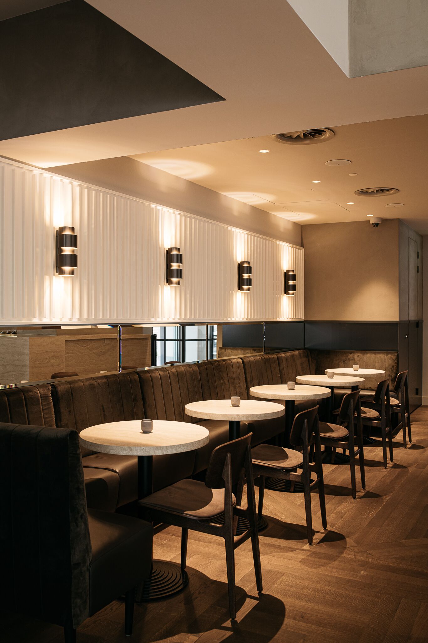 A modern restaurant interior with booth seating and round tables, featuring recessed lighting and a wooden floor.
