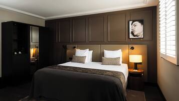 Une chambre d’hôtel avec un grand lit, une table de chevet avec une lampe, une armoire et une œuvre d’art accrochée au mur.