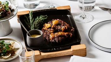 A dining table with a roasted meat dish, two glasses of red wine, and a small bowl of sauce.