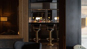 Una zona de bar con detalles en madera oscura, taburetes y una barra bien iluminada.
