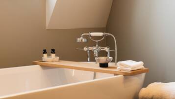 A modern bathroom with a freestanding bathtub, a wooden shelf with toiletries, and a black stool.