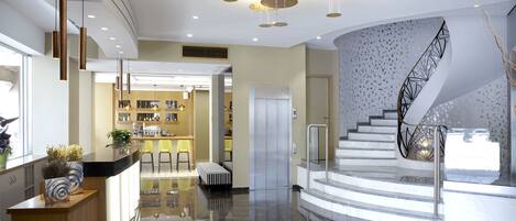 A modern hotel lobby with a central bar area, a staircase, and a reception desk.