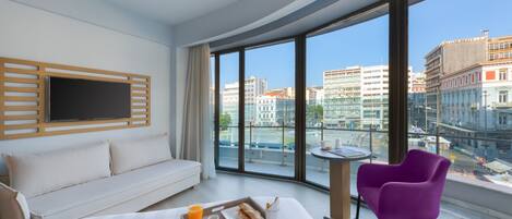 Une chambre d’hôtel avec un grand lit, un canapé, un fauteuil violet, un plateau de petit-déjeuner et un téléviseur fixé au mur.