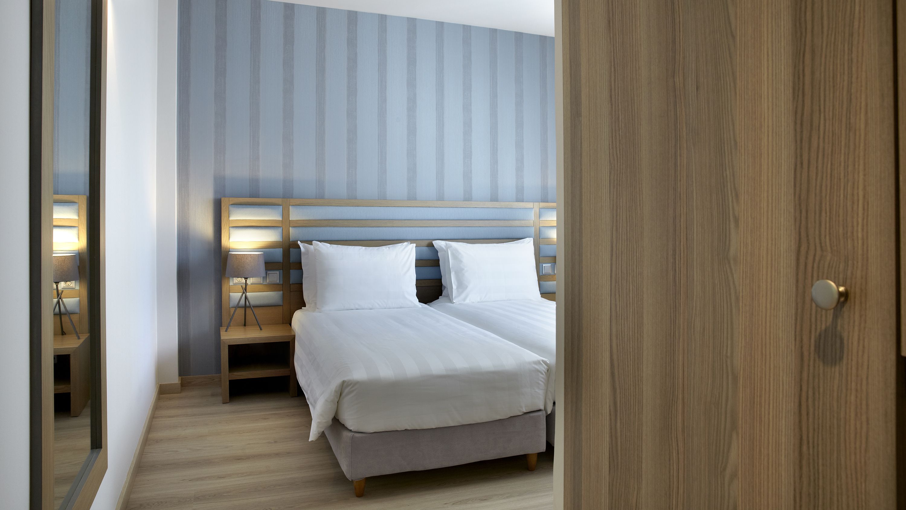 A hotel room with a bed, bedside tables, and a nightstand with lamps.