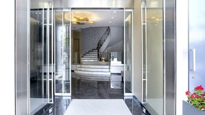 A modern hotel entrance with a glass door, a marble staircase, and a decorative ceiling light fixture.