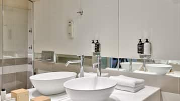 Une salle de bain moderne avec deux grands lavabos blancs, une douche en verre et un grand miroir.