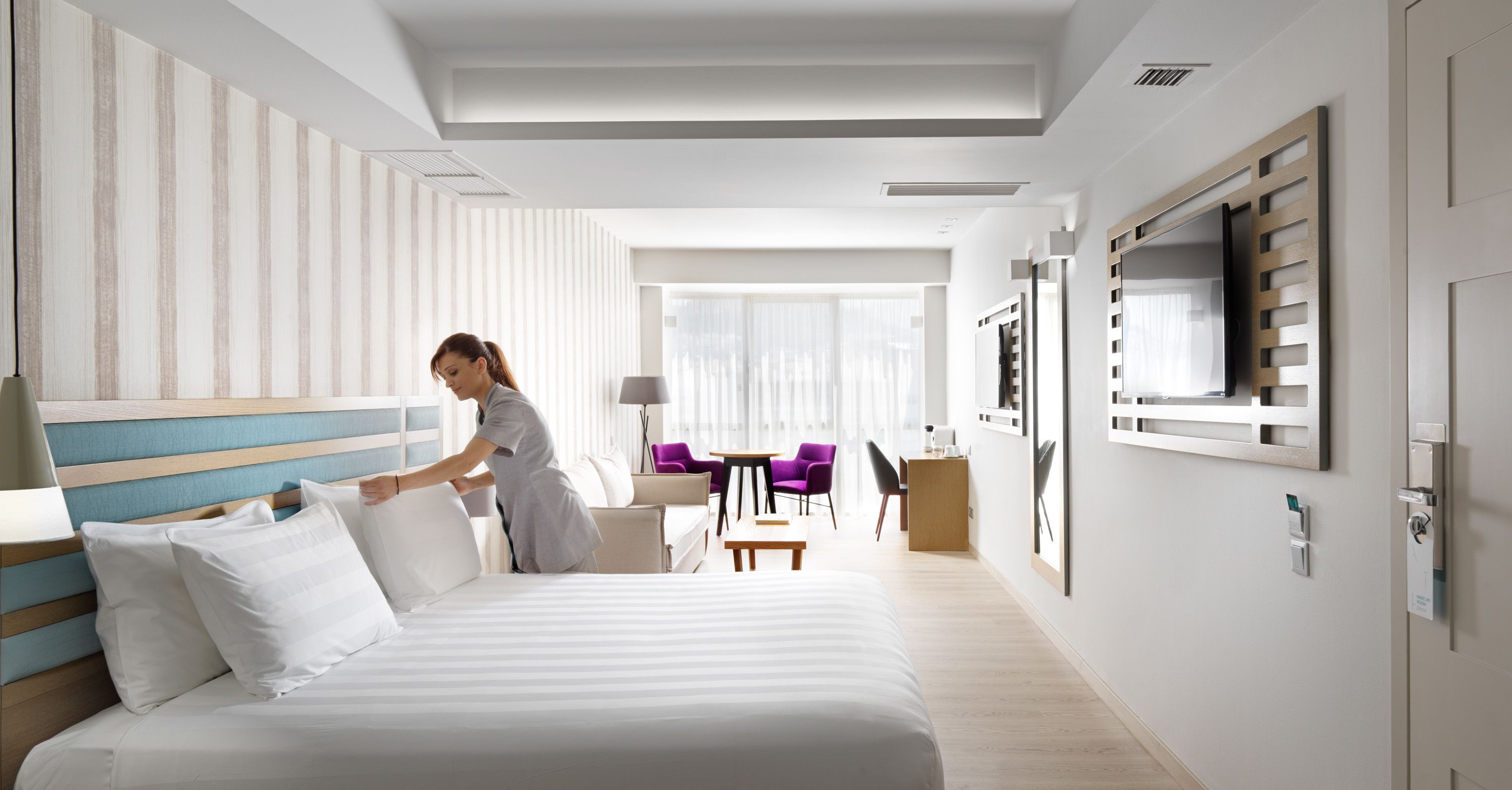 A hotel room with a bed, a desk, a chair, and a TV on the wall.