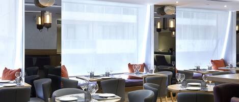 A modern restaurant with round tables, grey chairs, and large windows.