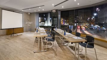 A conference room with a large screen, a podium, and a view of a cityscape at night.